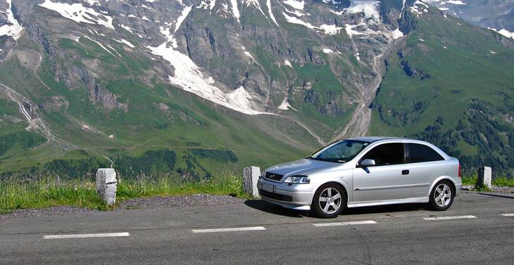 Siva Opel Astra parkirana na putu ispred planine